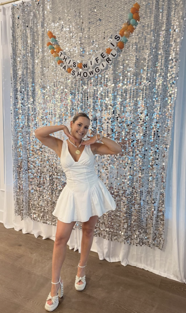 Sister Sunless client celebrating in a white dress before a silver sequin backdrop